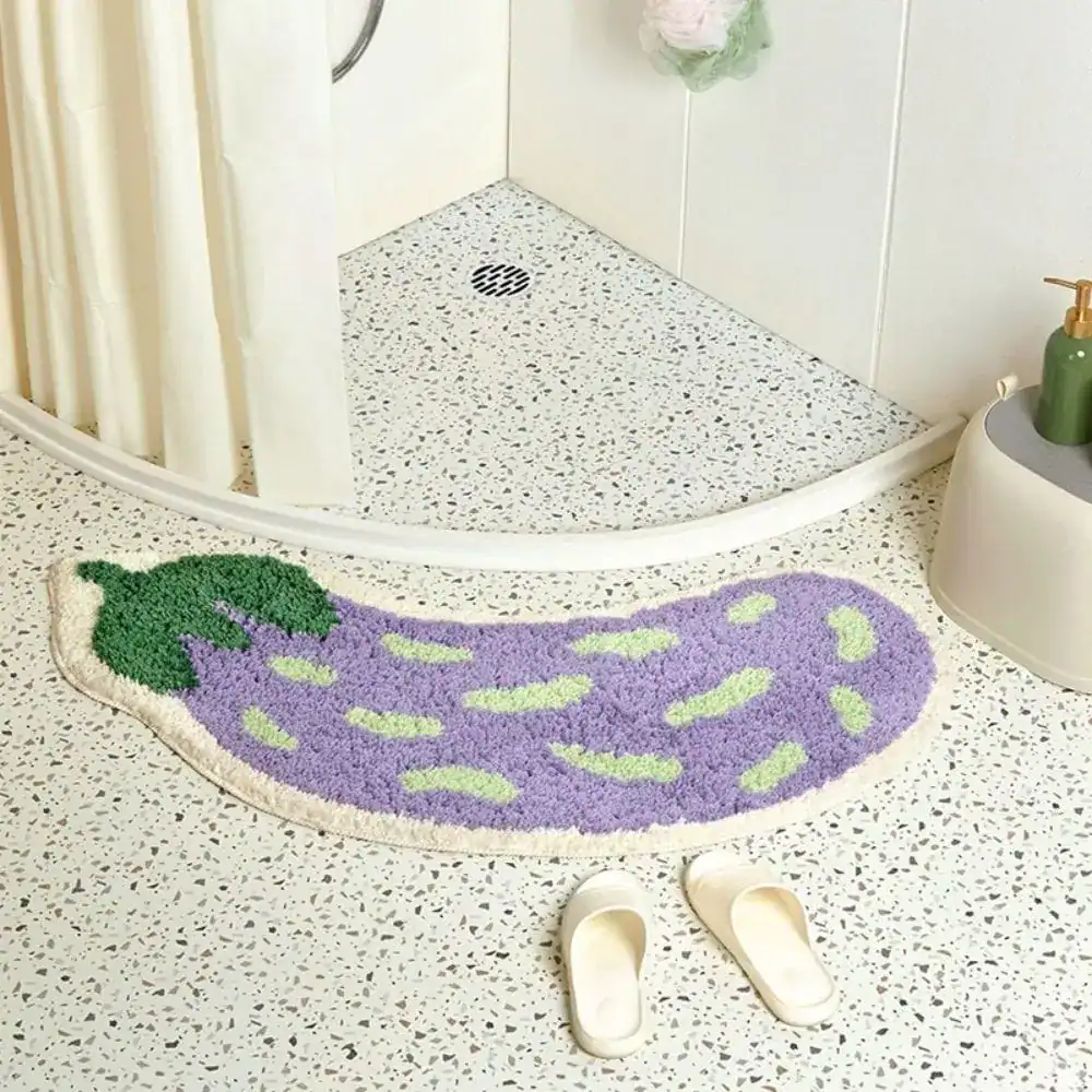 Badrumsmatta i auberginefärg, formad som en aubergine, med grön detalj och mjuk textur.