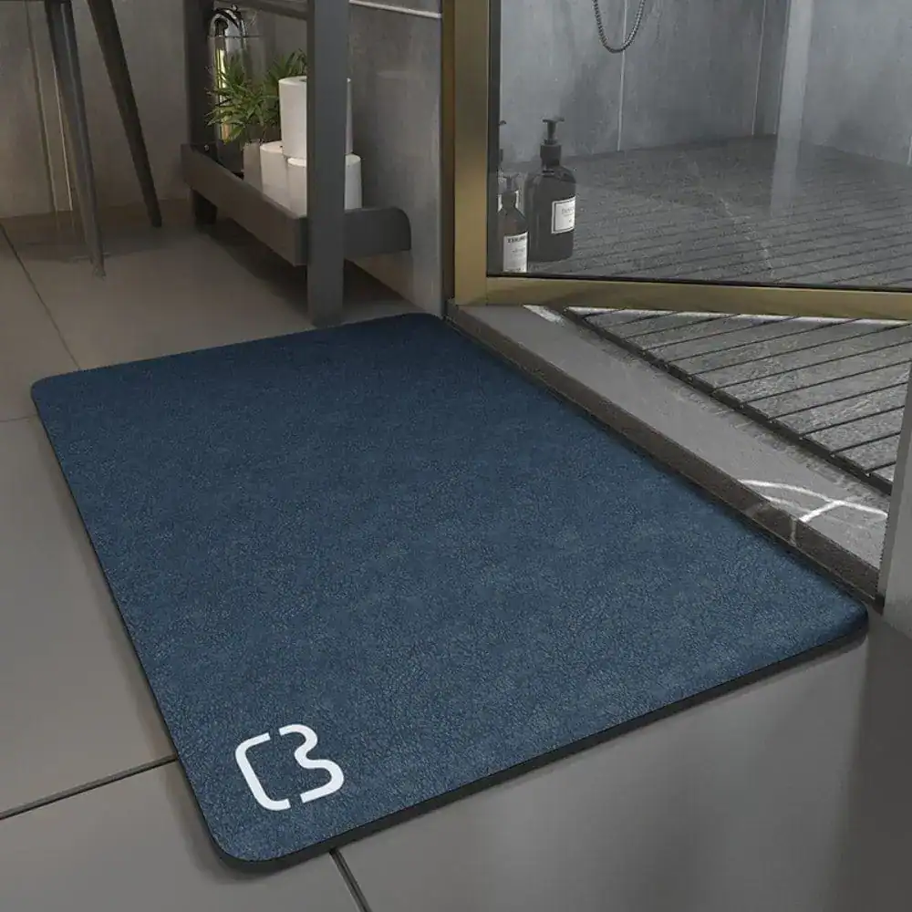 Blå badrumsmatta Diatomit Premium med vit logotyp, placerad vid duschen på kakelgolv.