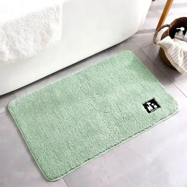 Mintgrön badrumsmatta med mjuk fluffig textur och svart logotyp på hörnet.