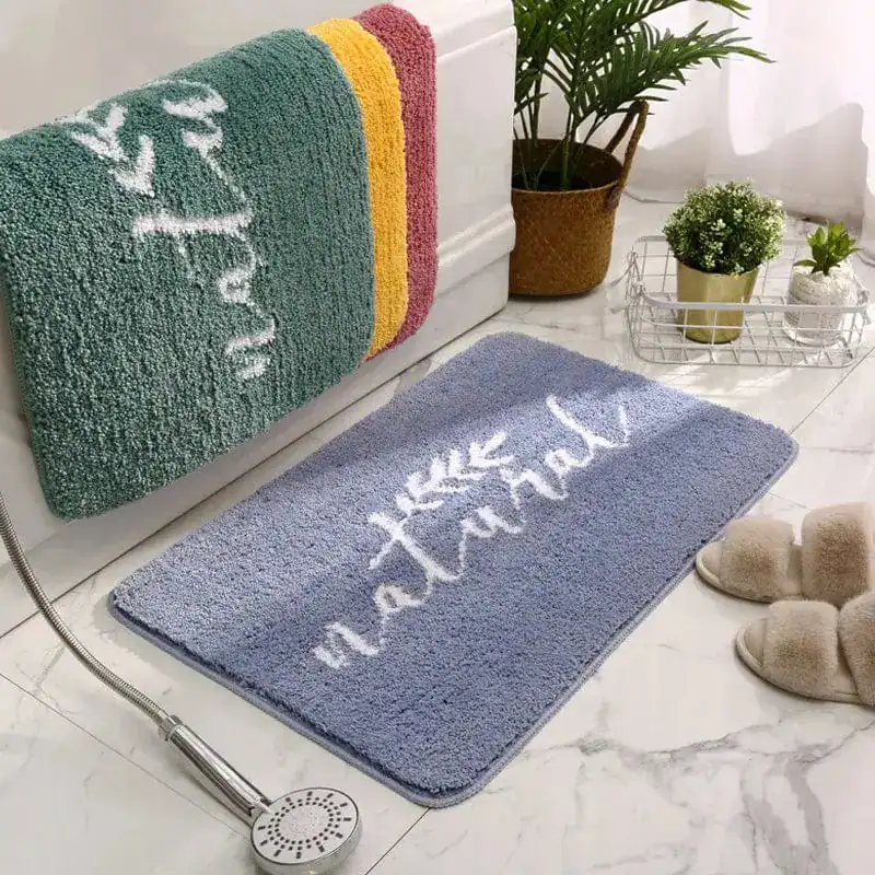 Badrumsmatta i blått med texten 'natural' och blad, i badrum med badrock och badslipper.