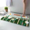 Grön badrumsmatta med vita kamomillblommor och texten 'Hello' i orange, i badrummet vid badkar.