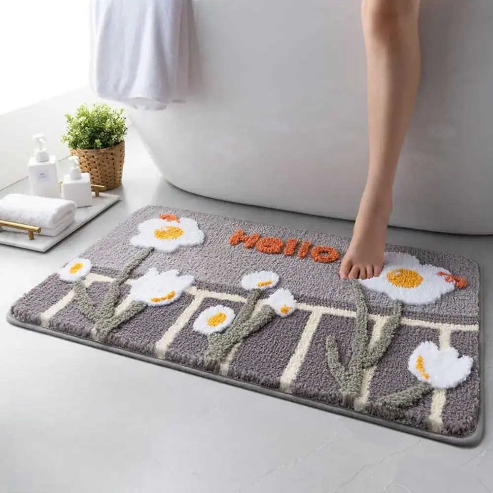 Grön badrumsmatta med vita blommor och texten 'Hello' i orange, i badrummet vid badkar.