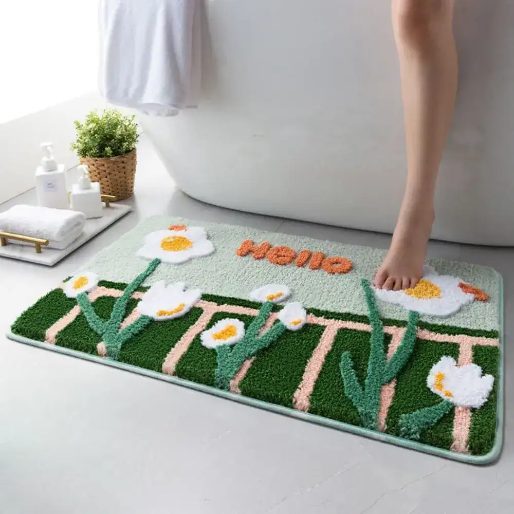 Grön badrumsmatta med vita kamomillblommor och texten 'Hello' i orange, i badrummet vid badkar.