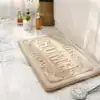 Beige badrumsmatta med präglat 'HOME' mönster, idealisk för badrummet.