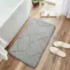 Grå kviltad badrumsmatta med geometrisk mönster, placerad vid badkar och trägolv.