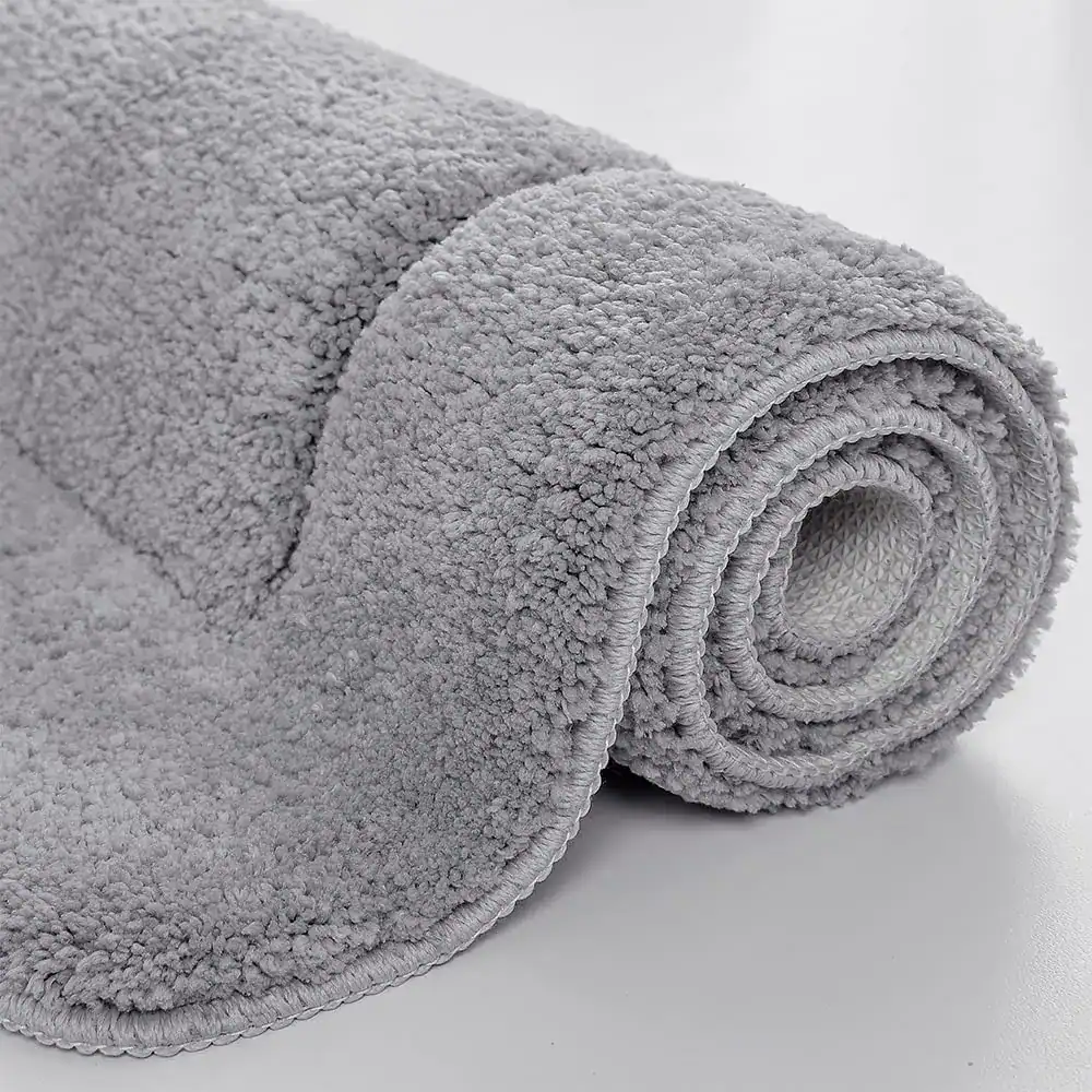 Stor badrumsmatta i grått, mjuk fluffig textil, rullad upp, idealisk för badrummet.